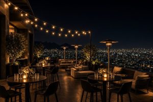 Festa de Aniversário Exclusiva em Cobertura no Belvedere – Belo Horizonte Cobertura sofisticada de prédio no bairro Belvedere, em Belo Horizonte, preparada para festa de aniversário à noite, com mesas bistrô altas, banquetas modernas, lounges confortáveis, aquecedores externos, luzes de corda e vista panorâmica das luzes da cidade.